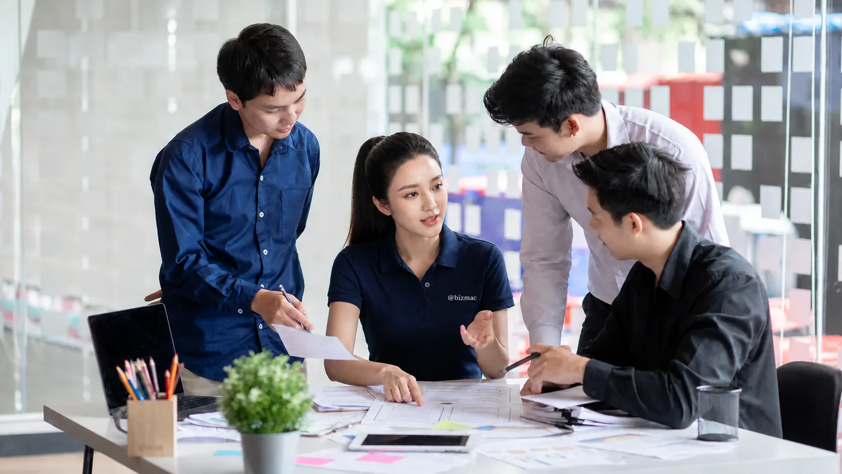 Đội thiết kế BizMaC ngồi quanh bàn tranh luận trên các bản wireframe vẽ tay của landing page
